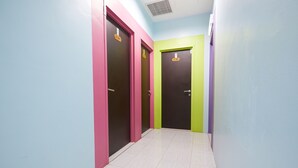 A hallway with three doors, each with a different color: pink, green, and purple. The walls are painted in light blue, and the floor is tiled. - Sy Jerantut Hotel (Jerantut)