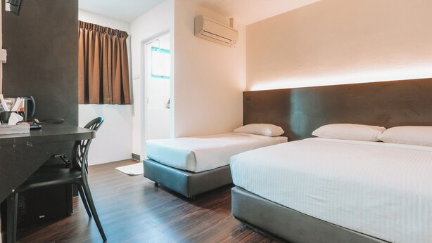 A hotel room with two single beds, a desk with a chair, a wardrobe, and an air conditioning unit. - A Hotel Desker (Singapore)