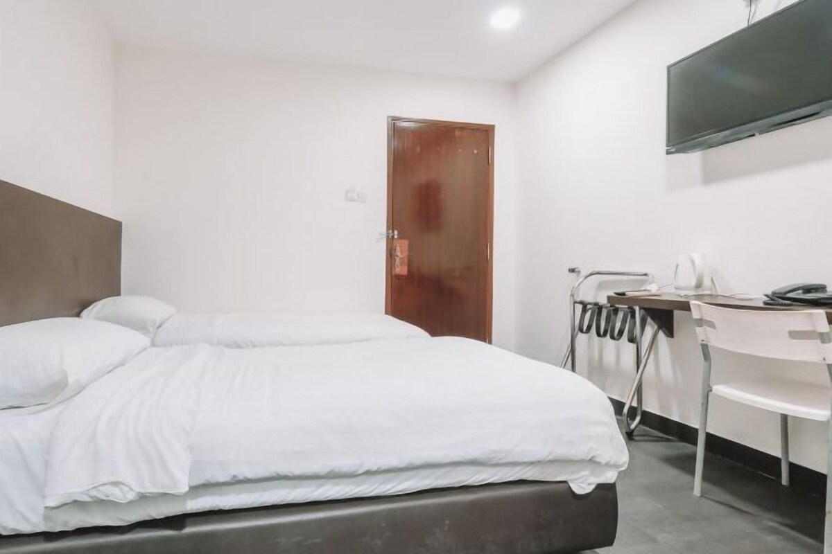 Una habitación de hotel con cama, escritorio, silla y televisor montado en la pared.