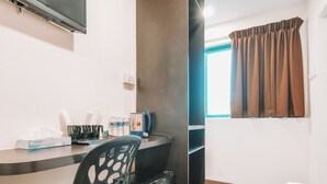 A compact hotel room with a kitchenette, a small table with a chair, a window with curtains, and a bed. - A Hotel Desker (Singapore)