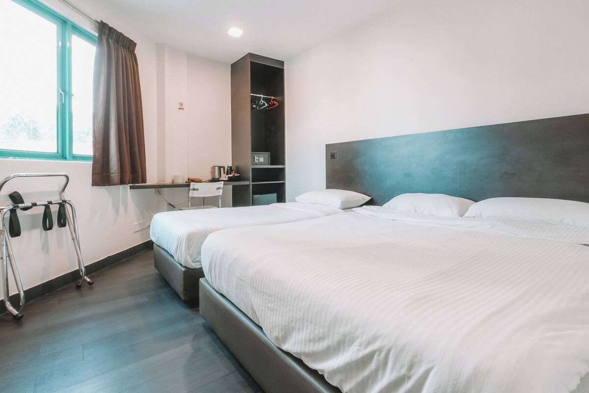 Habitación de hotel con dos camas, un escritorio, una silla, una mesita y una ventana con cortinas.