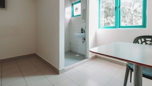 A room with a tiled floor, a window with teal frames, a sink, and a door leading to a bathroom. - A Hotel Desker (Singapore)