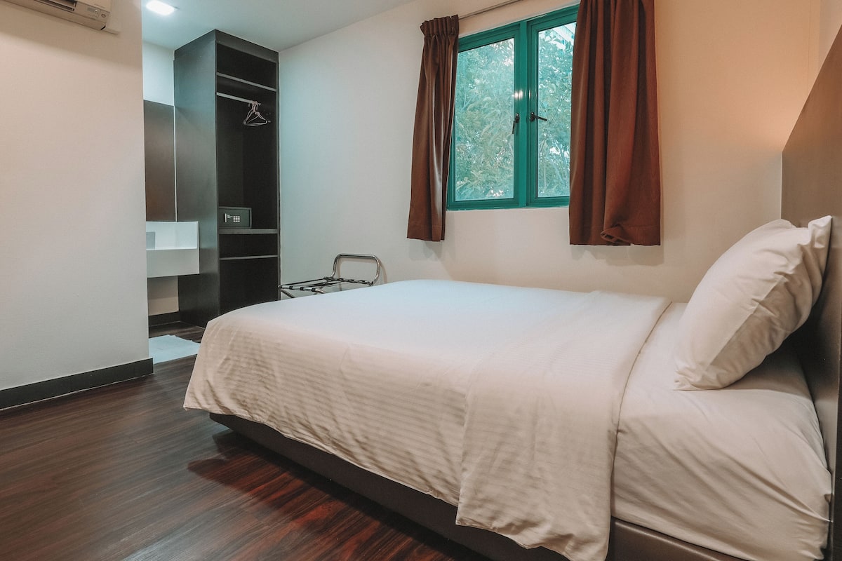 Un dormitorio con cama, armario, ventana con cortinas y una mesita.