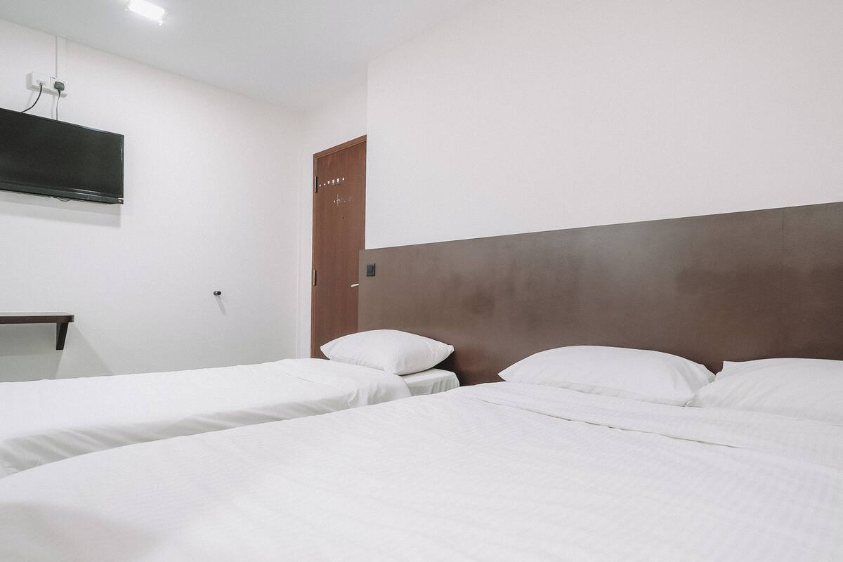 Habitación de hotel con dos camas individuales, una puerta de madera, un escritorio pequeño con una silla y un televisor de pantalla plana montado en la pared.