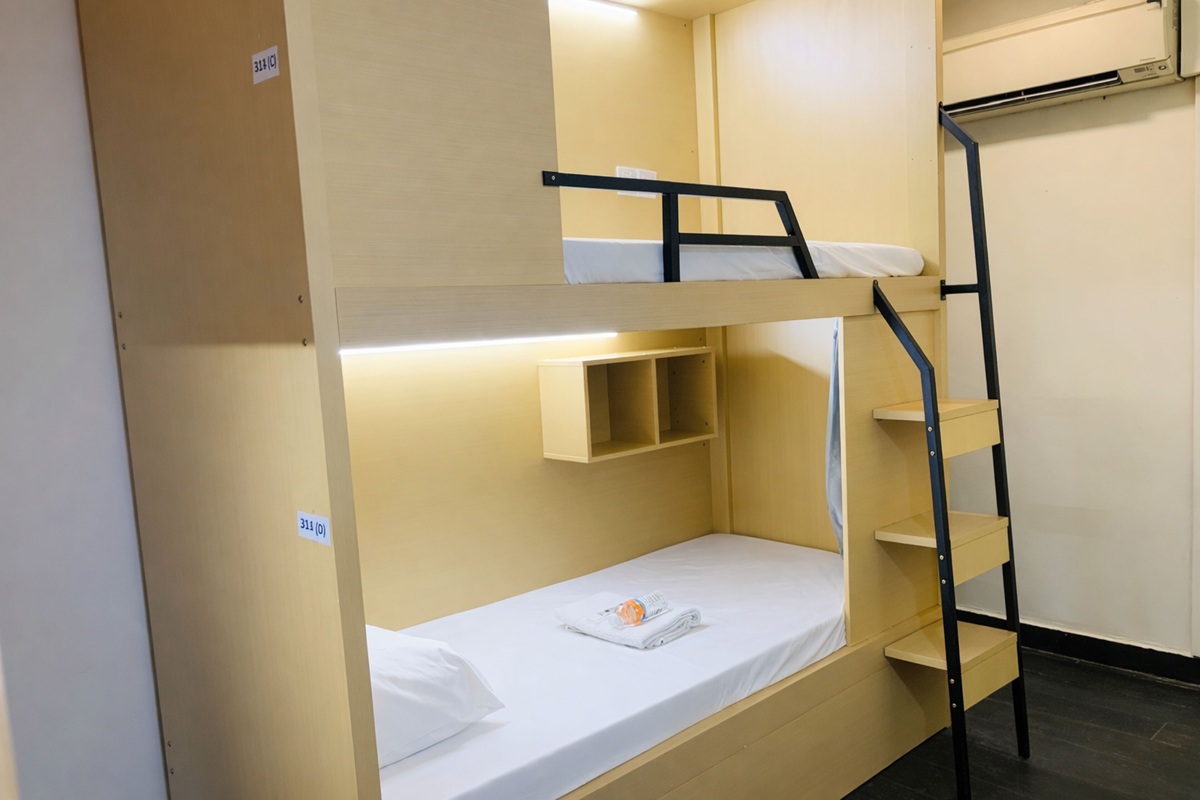 Una cama litera con un estante debajo de la cama superior y una escalera a un lado.