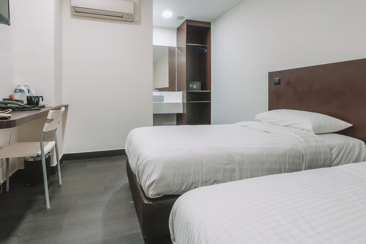 Habitación de hotel con dos camas, un escritorio, una silla, un armario y un equipo de aire acondicionado.