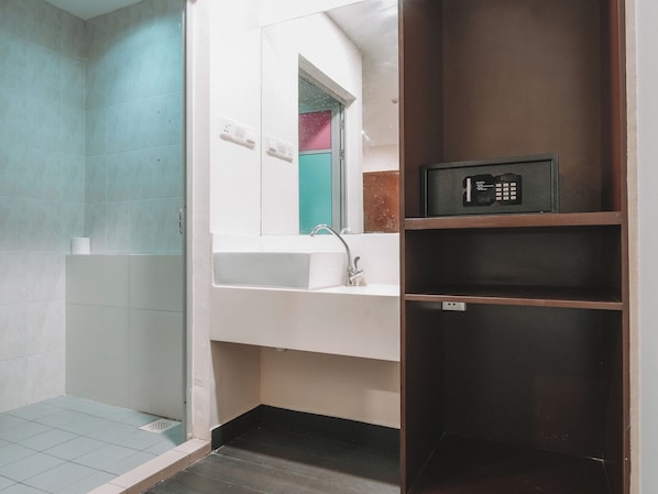 Baño con ducha, lavamanos y un panel de control de seguridad en un estante.