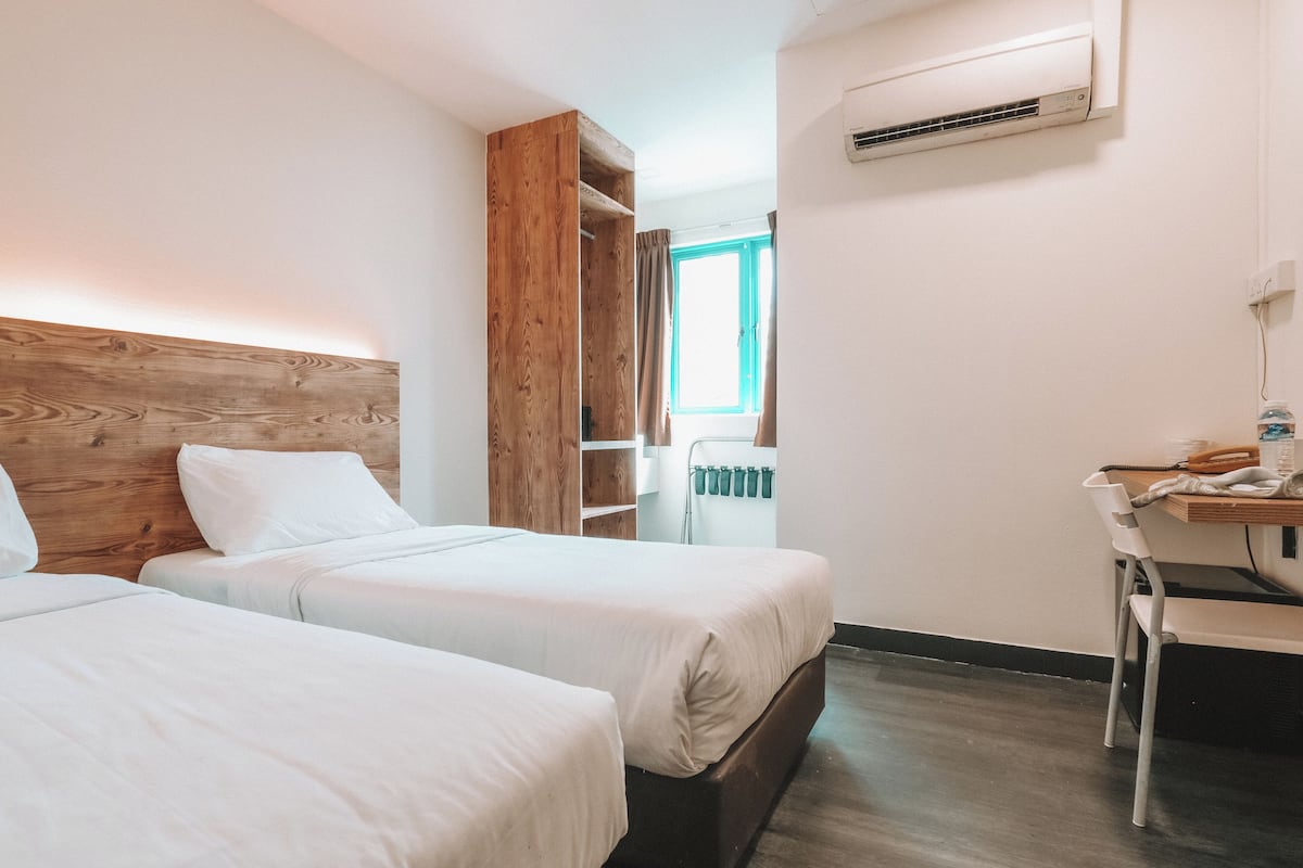Habitación de hotel con dos camas, cabecero de madera, escritorio y radiador.