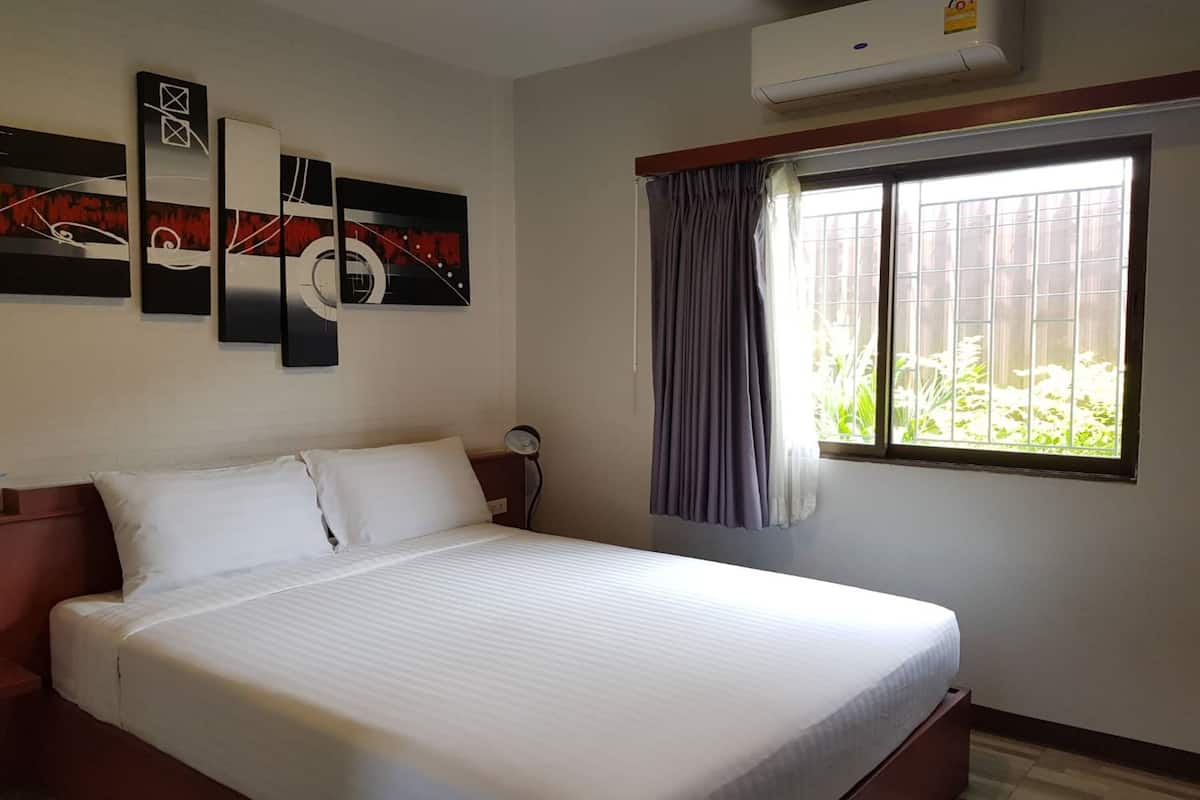 Hotelkamer met een bed, een wandairconditioner, een raam met gordijnen en abstracte wanddecoratie.