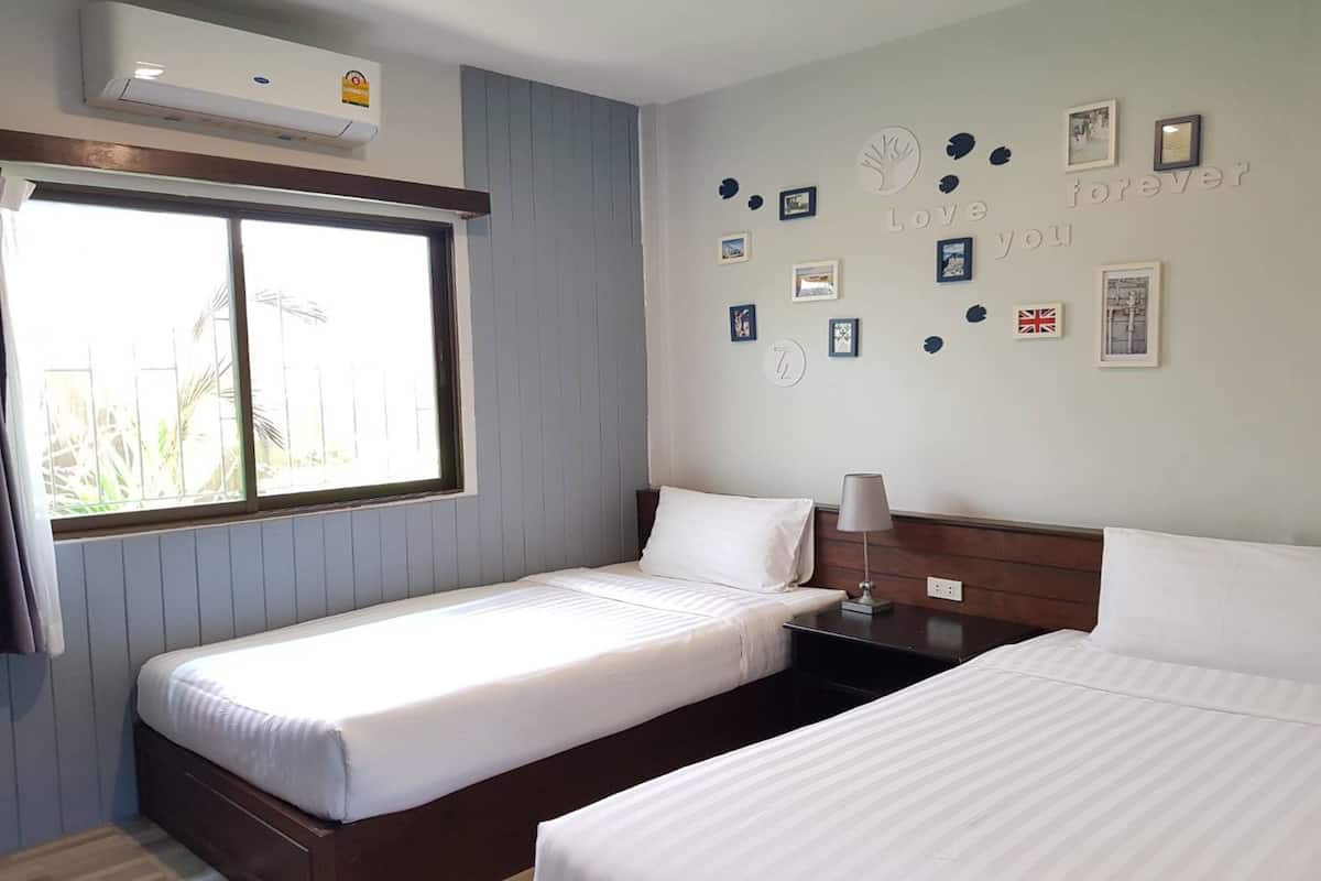 Een hotelkamer met twee enkele bedden, een raam en een muur versierd met ingelijste foto’s en een klok.