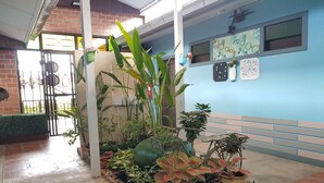 Een binnentuin met verschillende planten in potten, een betegelde vloer en een blauwe muur met decoratieve details.