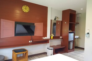 Ein Hotelzimmer mit Flachbildfernseher an der Wand, einem Holzschrank mit Spiegel, einer kleinen Mülleimer und einem Weidenhocker.