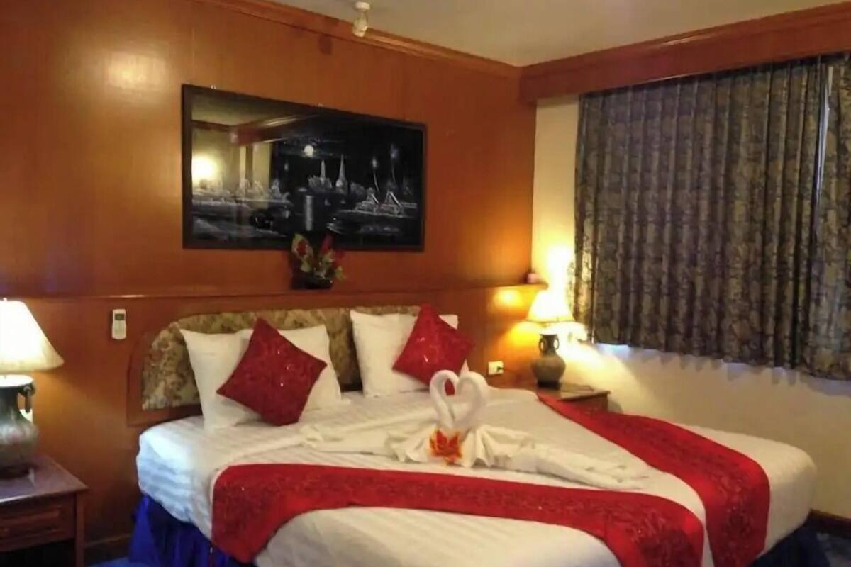 Una habitación de hotel con una cama, dos lámparas de noche, un cuadro en la pared y una ventana con cortinas.
