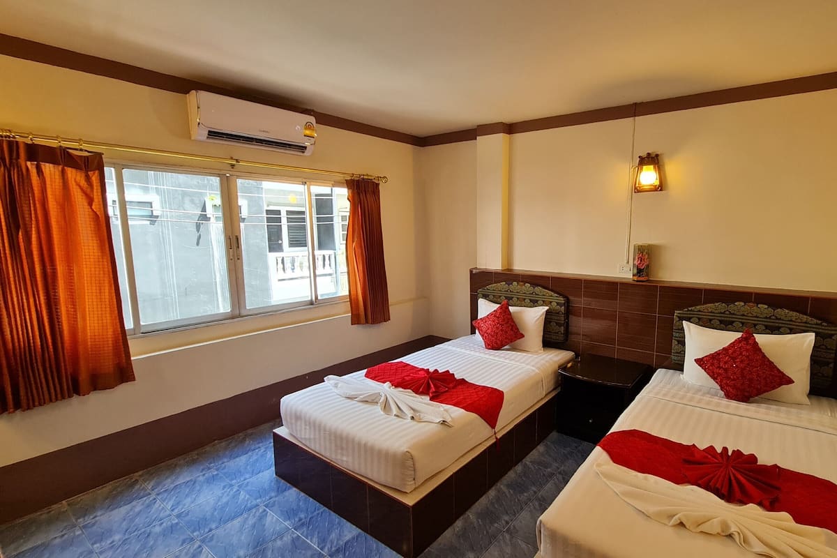 Una habitación de hotel con dos camas, una ventana con cortinas, un equipo de aire acondicionado e iluminación empotrada en la pared.
