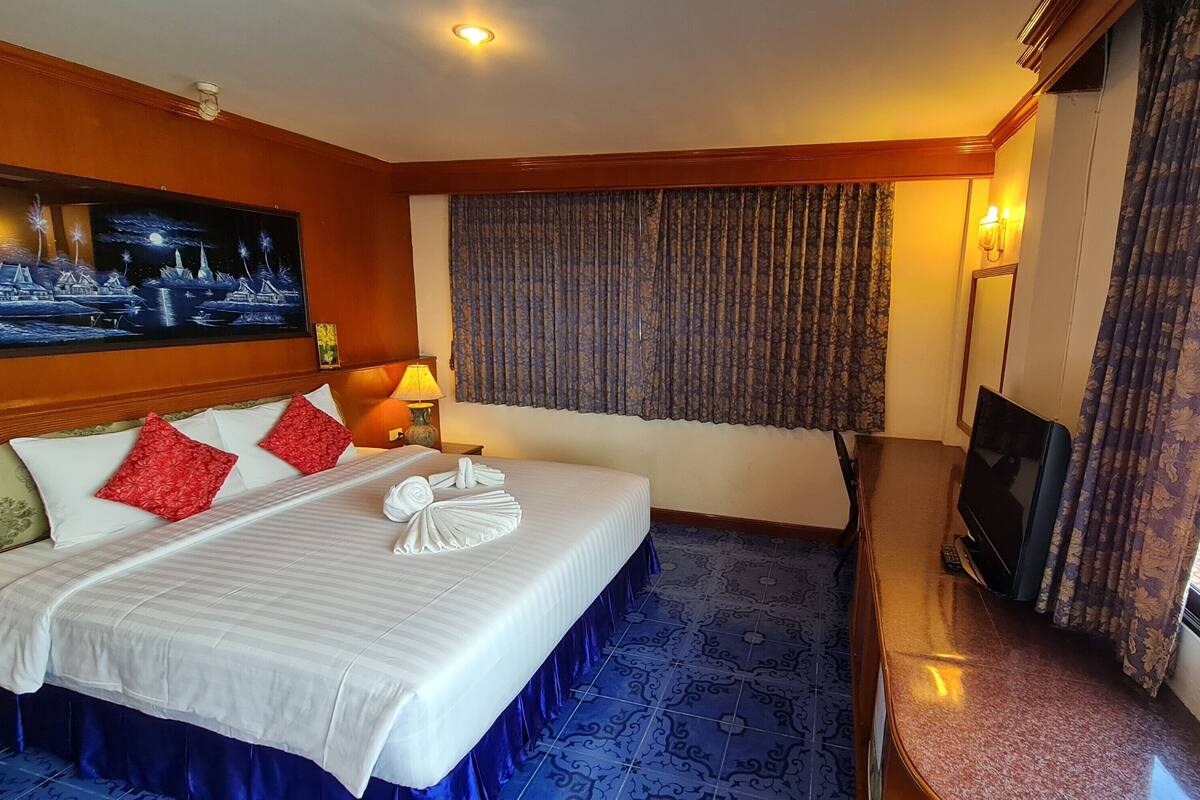 Habitación de hotel con una cama grande, un televisor de pantalla plana, un cuadro en la pared y una ventana con cortinas.