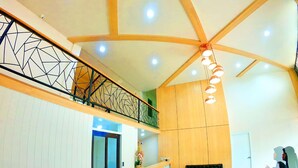 Eine geräumige Lobby mit hoher Decke, einem Empfangstresen, einem schwarzen Sofa und einer Treppe mit geometrischer Geländerkonstruktion.