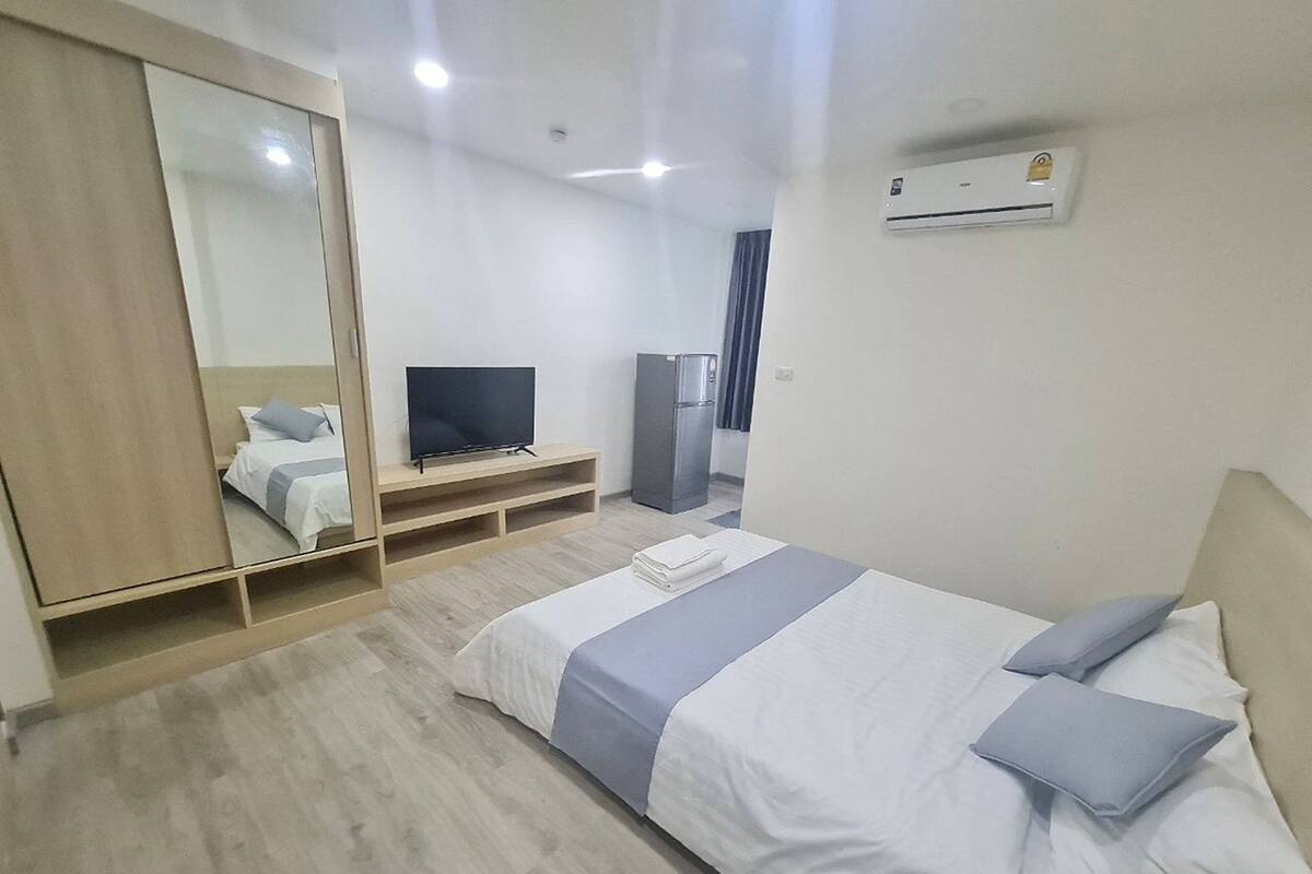 A hotel room with a bed, a TV, a wardrobe, and an air conditioning unit.