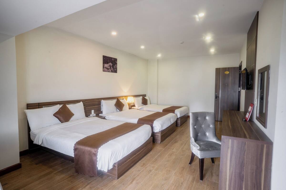 Une chambre d’hôtel avec trois lits, un bureau et une chaise.