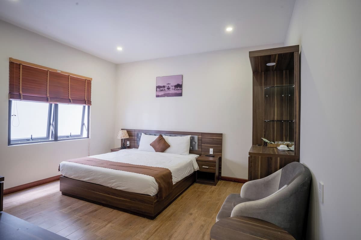 Une chambre à coucher avec un lit en bois, une table de chevet, une chaise, une armoire et une fenêtre avec des stores.