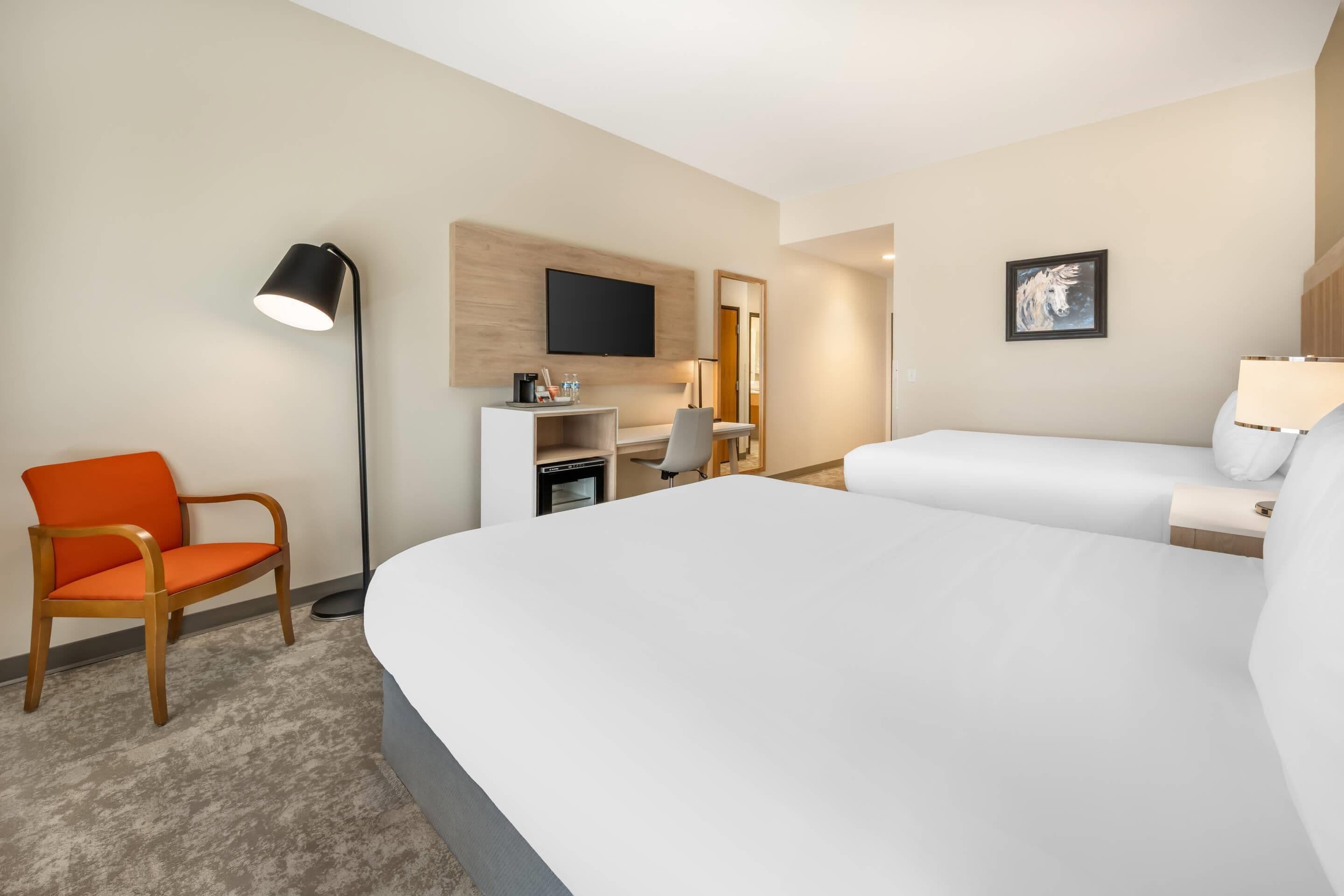 A hotel room with a large bed, a desk with a chair, a TV mounted on the wall, and a small table with a lamp.