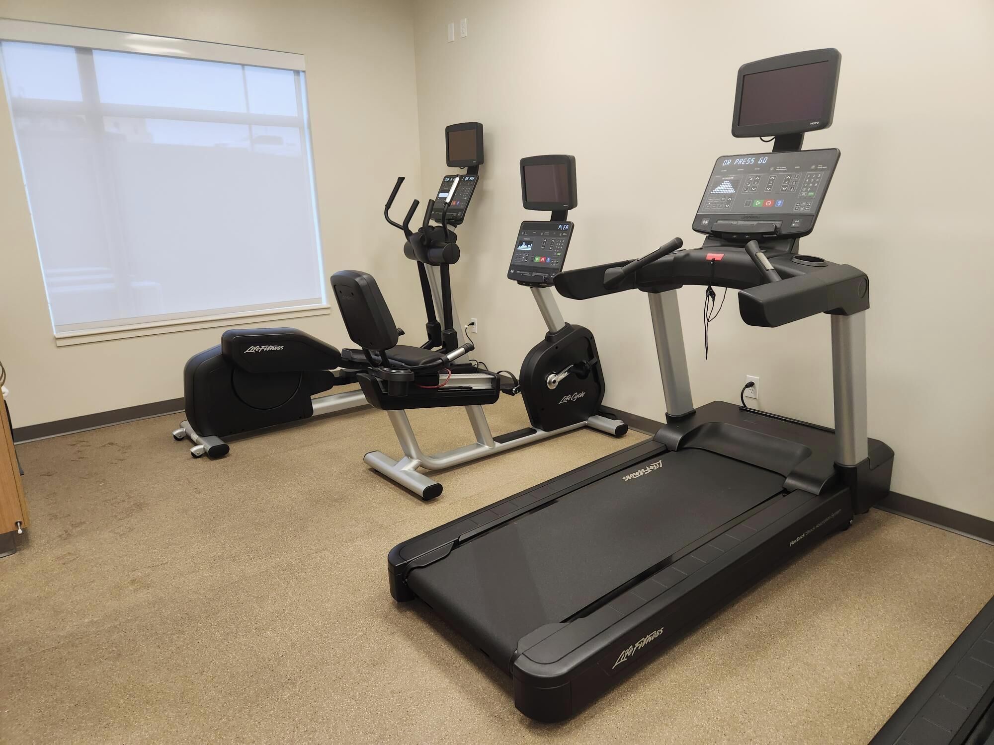Et fitnessrum med træningsmaskiner, herunder løbebånd, crosstrainer og motionscykel.