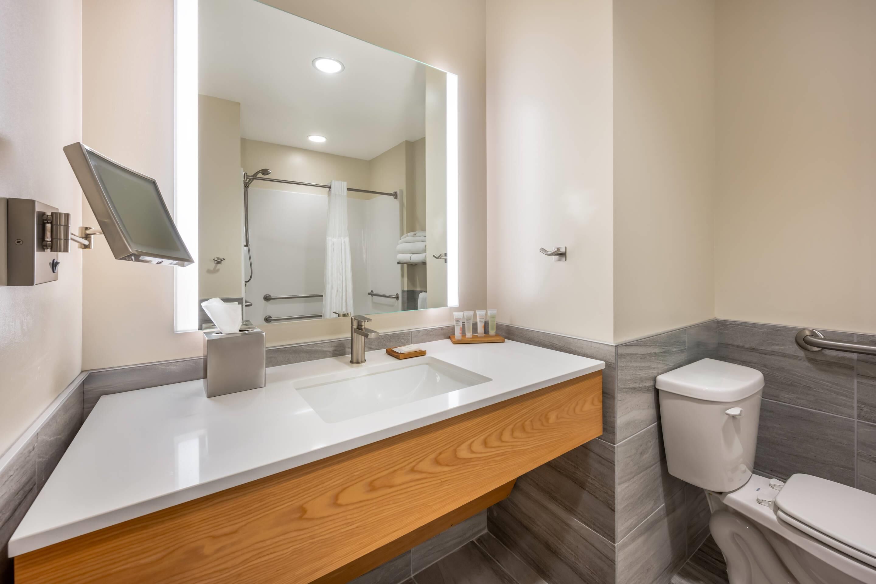 A modern bathroom with a white sink, wooden vanity, a large mirror, and a toilet.