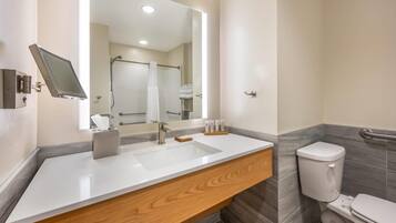A modern bathroom with a white sink, wooden vanity, a large mirror, and a toilet.