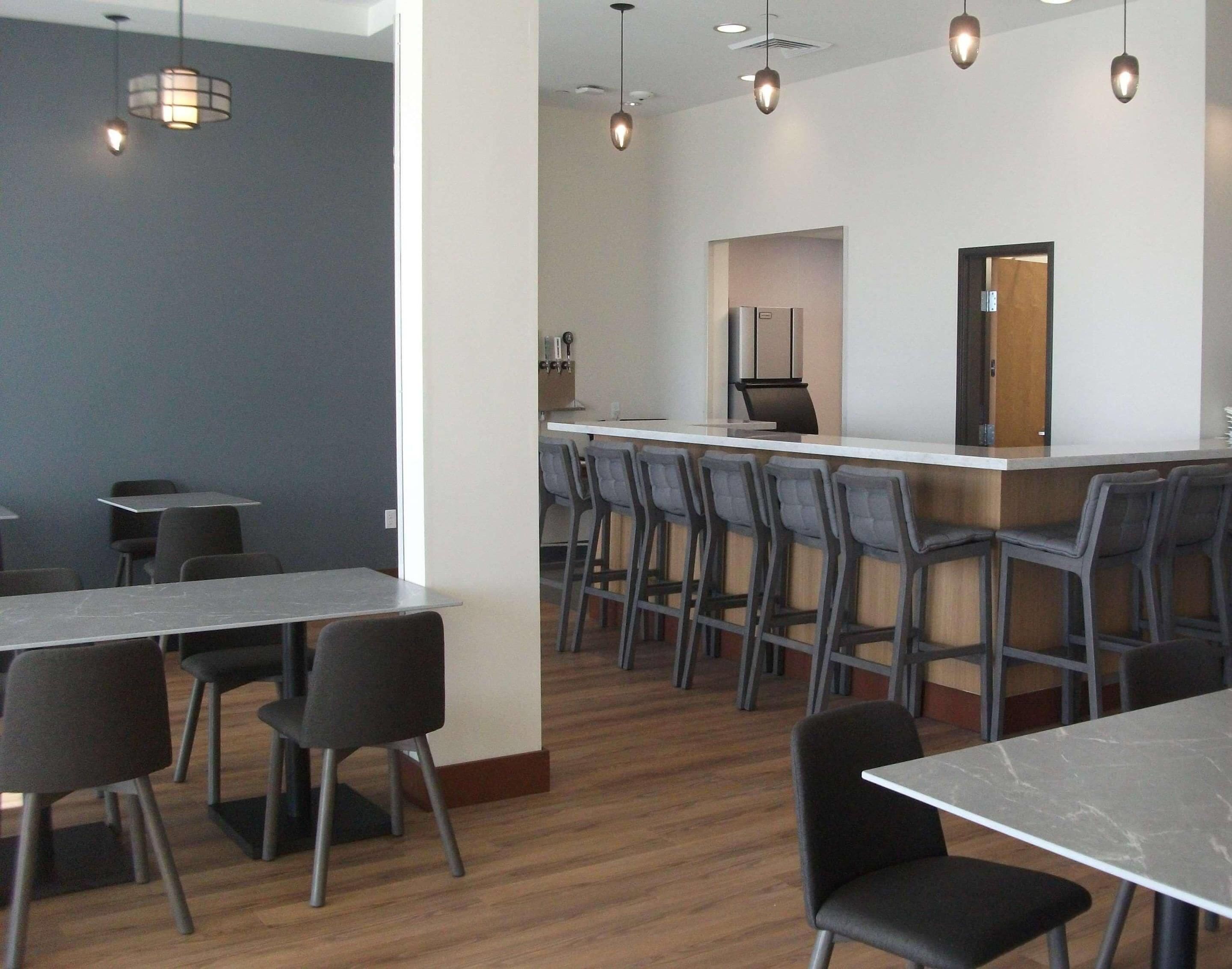 A modern dining area with high tables and bar stools, a kitchen area with a refrigerator, and pendant lighting.