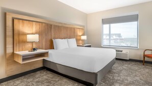 A modern hotel room with a large bed, wooden headboard, bedside tables with lamps, a large window with a view, and a carpeted floor. - Radisson Hotel Pendleton Airport (Pendleton)