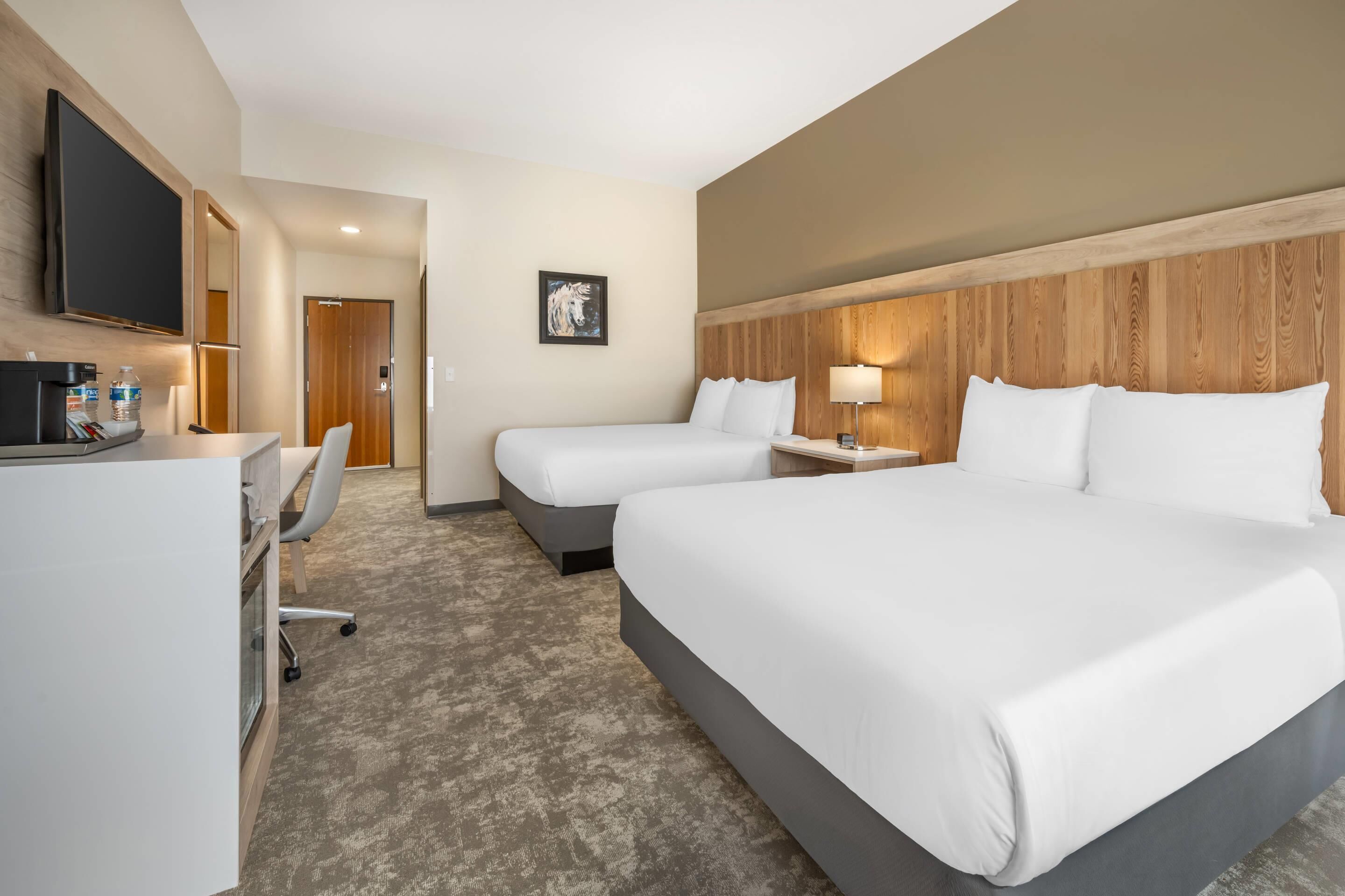A hotel room with two beds, a desk, a chair, a TV, and a painting on the wall.