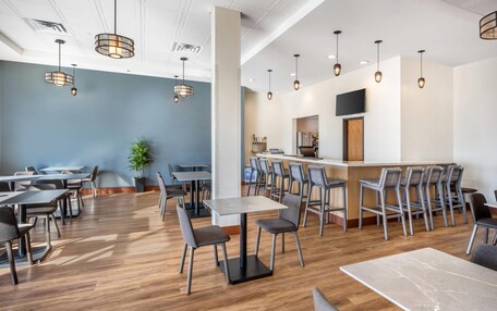 A modern dining area with wooden flooring, multiple tables and chairs, and pendant lighting.