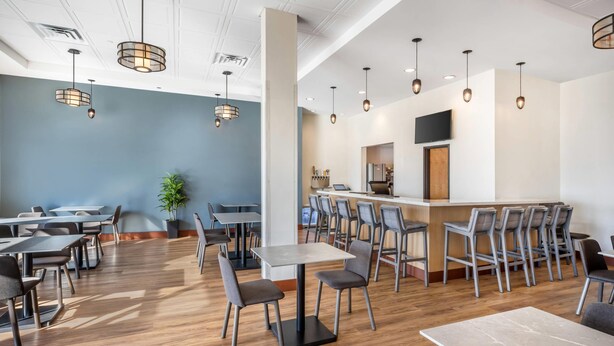 A modern dining area with wooden flooring, multiple tables and chairs, and pendant lighting. - Radisson Hotel Pendleton Airport (Pendleton)