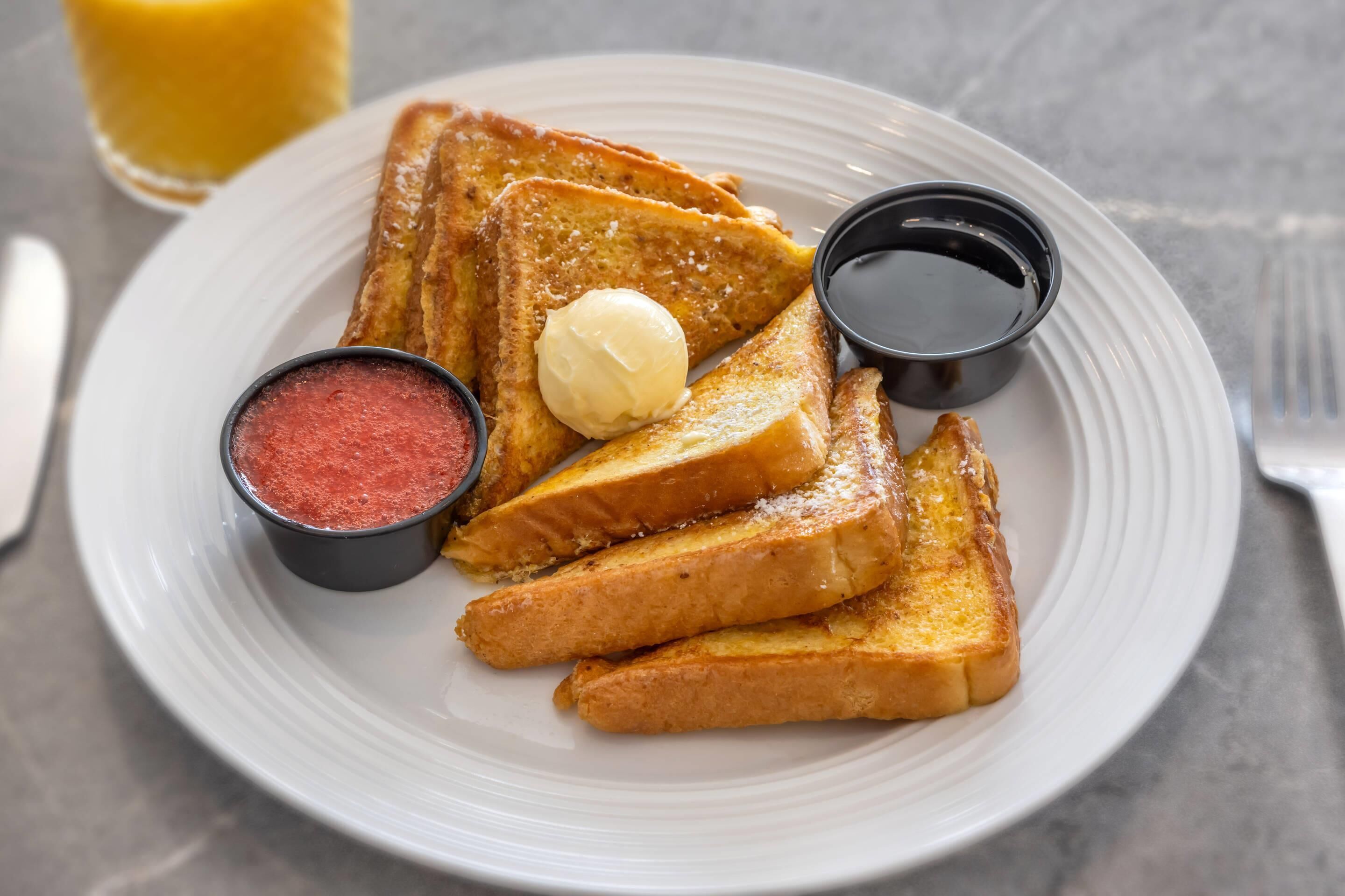 A plate of French toast with butter, syrup, and powdered sugar.