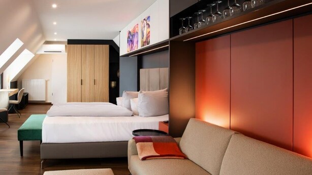 A modern hotel room with two beds, a sofa, and a dining table. - Design- und Kunsthotel München (Munich)
