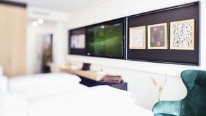 A modern living room with a large flat-screen TV, a wooden coffee table, and a green armchair. - Design- und Kunsthotel München (Munich)