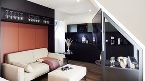A modern living room with a sofa, ottoman, and a glass partition. - Design- und Kunsthotel München (Munich)