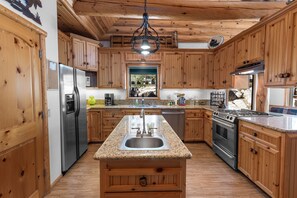 A kitchen with wooden cabinets, stainless steel appliances, granite countertops, and a central island with a sink.