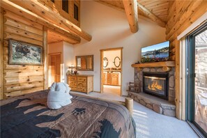 A log cabin interior with a bed, fireplace, wooden walls, and a television.