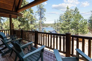 Um deck de madeira com cadeiras Adirondack com vista para um lago e floresta.