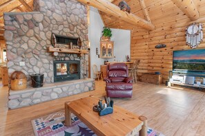 A cozy log cabin interior with a stone fireplace, leather recliner, and a large TV.