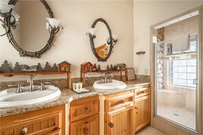 A bathroom with two sinks, wooden cabinets, a shower with a stone wall, and decorative mirrors.