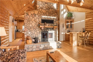 A cozy cabin interior with a stone fireplace, wooden furniture, and a kitchen area. - 5-STAR 2,086 sq ft LOG CABIN with LAKE VIEWS & Game room. In Boulder Bay! (Big Bear Lake)
