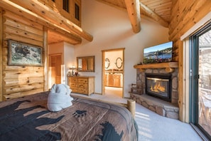 A log cabin interior with a bed, fireplace, wooden walls, and a television. - Luxury Log Cabin with Lake Views & Game Room | 2,000 sq ft home (Big Bear Lake)