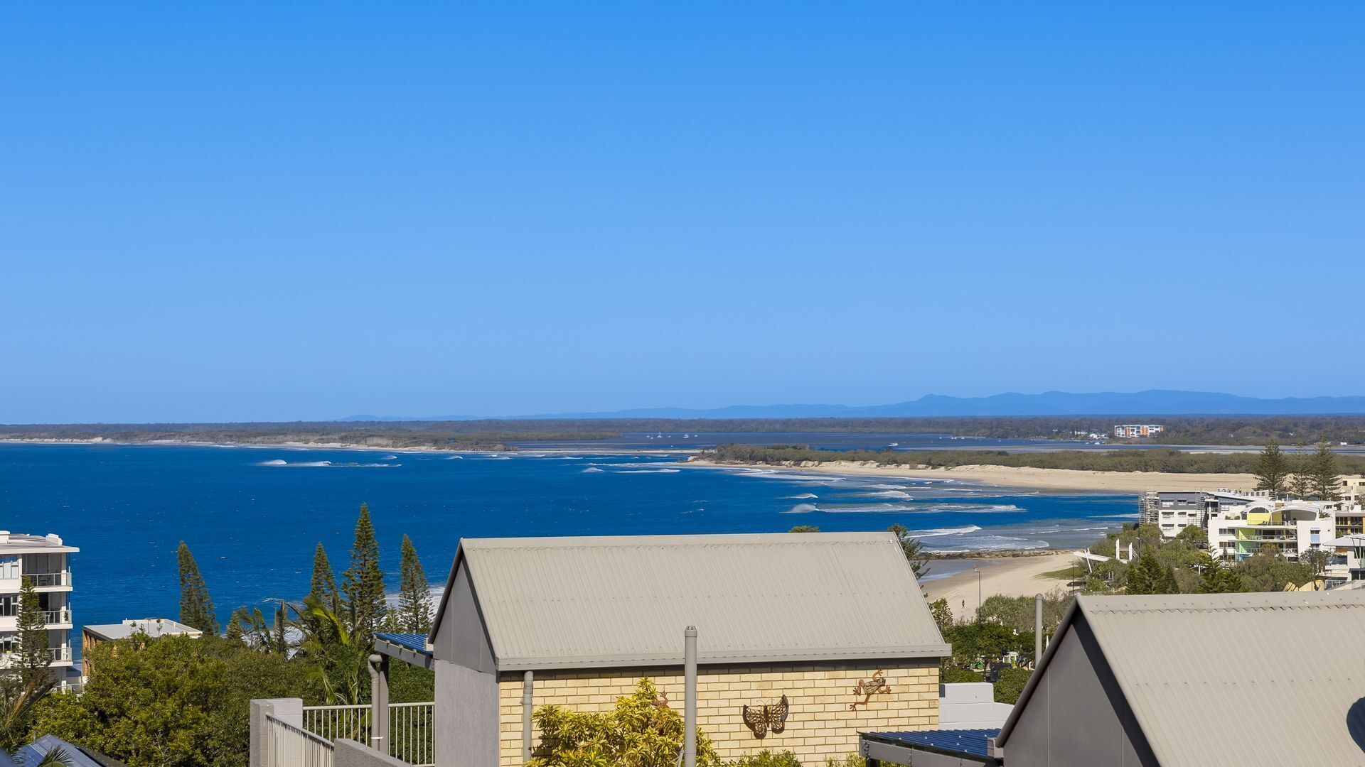 Une vue sur la côte, avec un ciel dégagé, une plage de sable et une chaîne de montagnes à l’horizon.