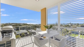 Ein Balkon mit Grill, weißen Korbmöbeln und einem Blumentopf.