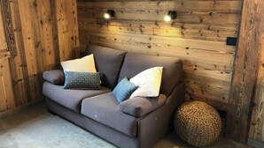 A modern living room with a grey sofa, two patterned cushions, and a round woven stool. - Wifi, Ground floor, view mountain, terrace, parking, ski locker, 40m², Le Grand Bornand (Le Grand-Bornand)