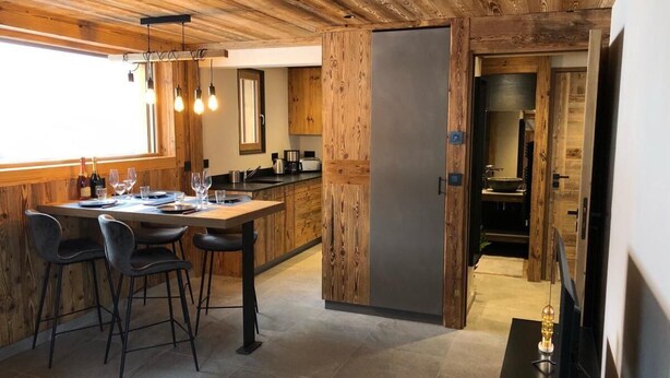 A modern kitchen with wooden accents, a dining area with chairs, and a large window providing natural light. - Wifi, Ground floor, view mountain, terrace, parking, ski locker, 40m², Le Grand Bornand (Le Grand-Bornand)