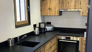 A modern kitchen with wooden cabinets, a black countertop, a built-in oven, and a window with blinds. - Wifi, Ground floor, view mountain, terrace, parking, ski locker, 40m², Le Grand Bornand (Le Grand-Bornand)