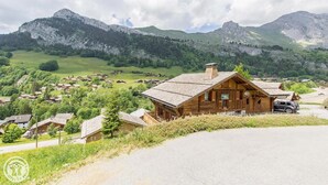 A wooden mountain lodge with a sloped roof, surrounded by a village and mountains. - Wifi, 50m from ski slopes, Ground floor, view mountain, terrace, fireplace or stove, parking, 55m² (Le Grand-Bornand)