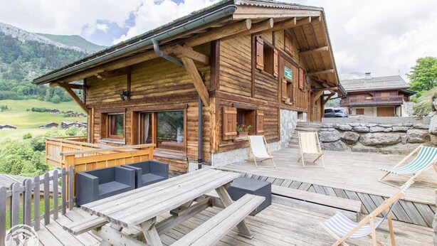 A wooden chalet with a deck, outdoor seating, and a scenic mountain view. - Wifi, 50m from ski slopes, Ground floor, view mountain, terrace, fireplace or stove, parking, 55m² (Le Grand-Bornand)